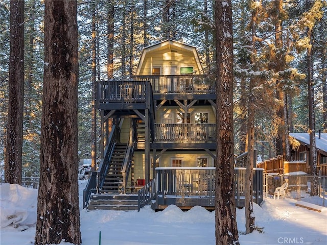 snow covered property with a gambrel roof, a deck, and stairs