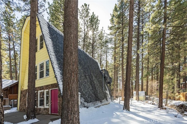 snow covered property featuring stone siding and a shingled roof