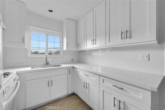 kitchen with light countertops, white gas range oven, a sink, and white cabinets