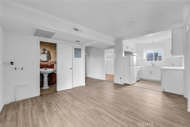 unfurnished living room featuring electric panel, visible vents, a sink, and light wood-style flooring