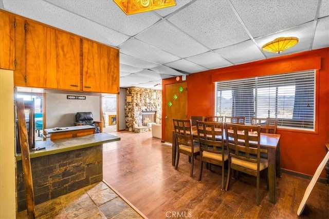 dining area featuring a paneled ceiling, a fireplace, baseboards, and wood finished floors