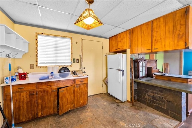 kitchen with a paneled ceiling, light countertops, freestanding refrigerator, brown cabinets, and decorative light fixtures