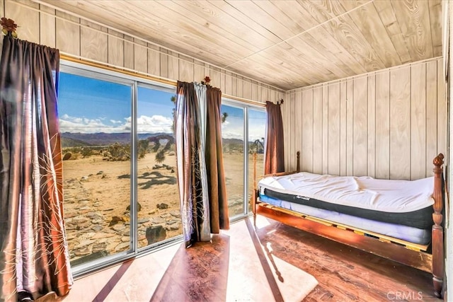 bedroom with wooden walls, wooden ceiling, wood finished floors, access to exterior, and a mountain view