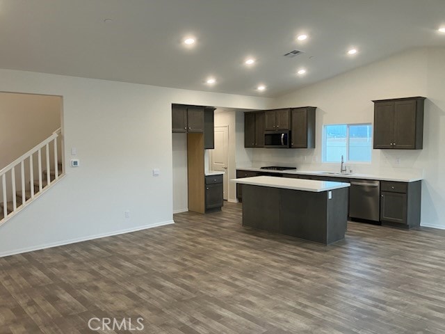 kitchen with dark wood finished floors, lofted ceiling, appliances with stainless steel finishes, a center island, and a sink