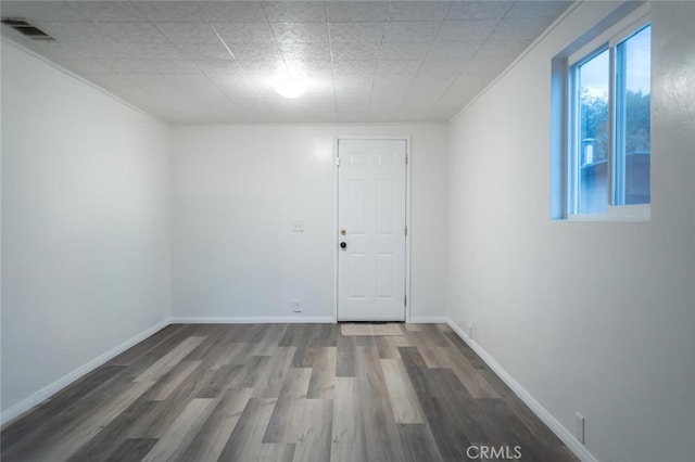 unfurnished room with plenty of natural light, wood finished floors, visible vents, and baseboards