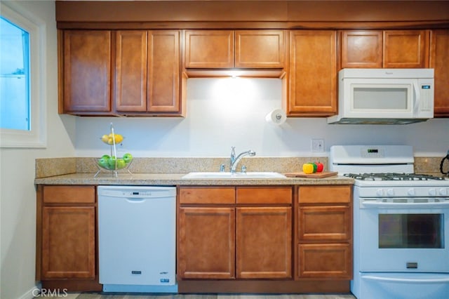 kitchen with light stone countertops, white appliances, brown cabinetry, and a sink