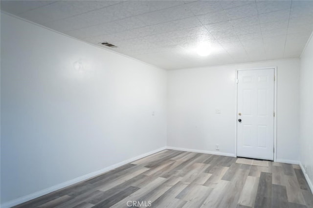 empty room featuring wood finished floors, visible vents, and baseboards