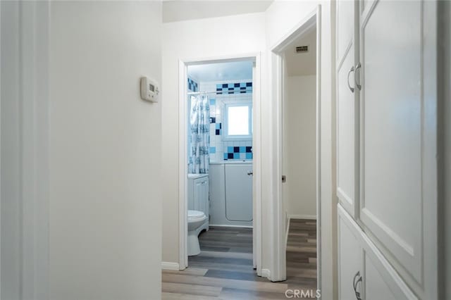 hall with light wood finished floors, visible vents, and baseboards