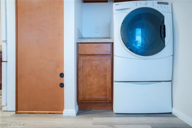 laundry room featuring light wood-type flooring, washer / dryer, baseboards, and cabinet space