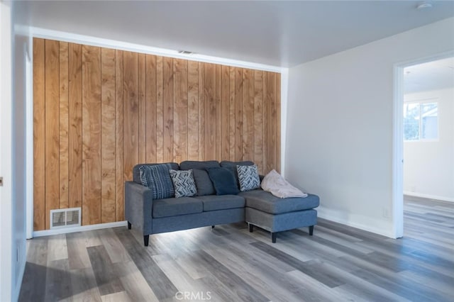 living area featuring wood walls, baseboards, visible vents, and wood finished floors