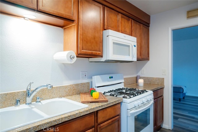 kitchen featuring light countertops, white appliances, a sink, and brown cabinets