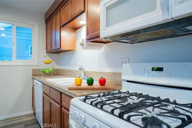 kitchen with white appliances, baseboards, brown cabinetry, light countertops, and a sink