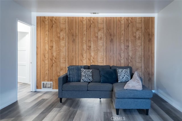 living area featuring baseboards, wood finished floors, visible vents, and wooden walls