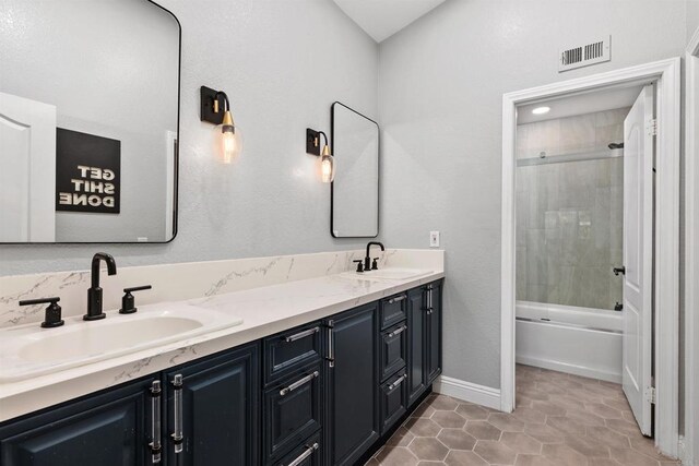 full bathroom featuring double vanity, combined bath / shower with glass door, visible vents, and a sink