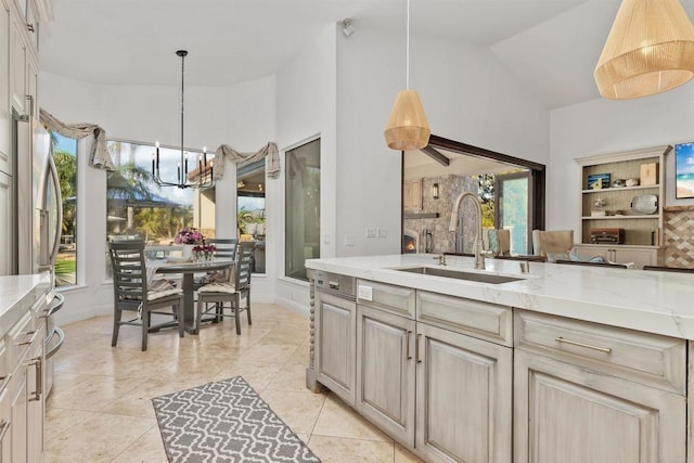 kitchen with a sink, decorative light fixtures, light stone counters, an inviting chandelier, and vaulted ceiling