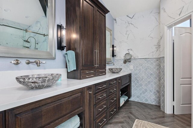 bathroom featuring a sink, a marble finish shower, tile walls, and double vanity