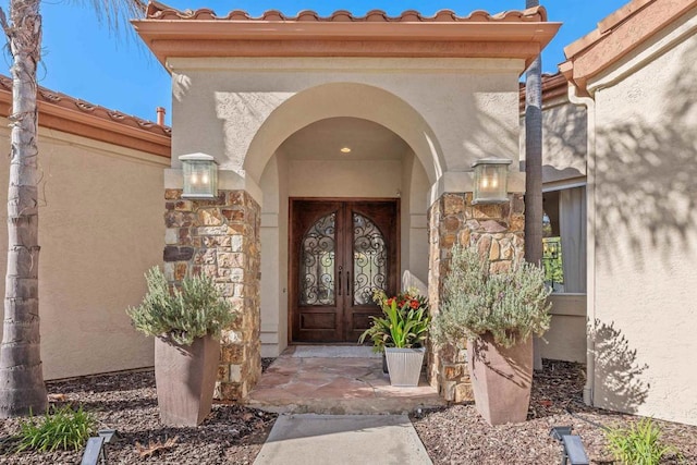 doorway to property featuring a tiled roof, french doors, stone siding, and stucco siding