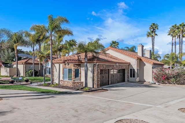 mediterranean / spanish house with an attached garage, a chimney, concrete driveway, stone siding, and a tiled roof