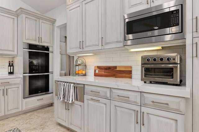 kitchen with decorative backsplash, light stone counters, a toaster, and appliances with stainless steel finishes