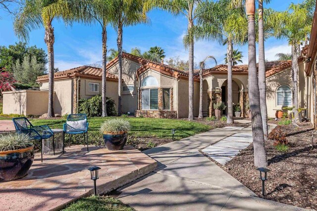 back of property featuring stucco siding, a patio, a lawn, and a tiled roof