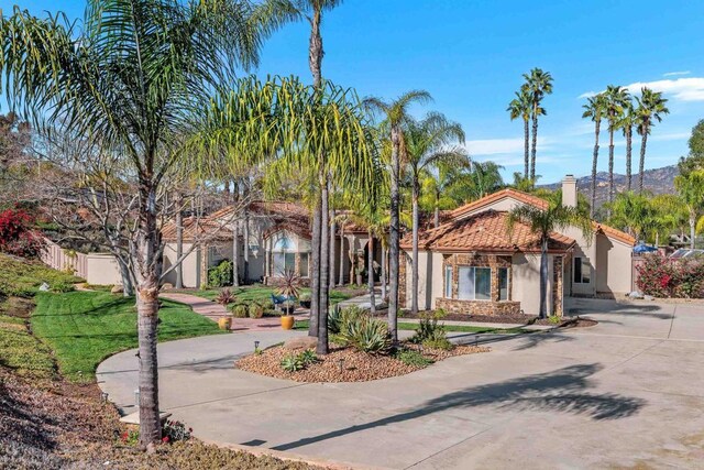 view of front of property featuring stucco siding, concrete driveway, a chimney, and a tile roof