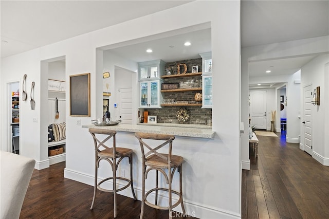 kitchen featuring a breakfast bar area, open shelves, dark wood-style flooring, glass insert cabinets, and tasteful backsplash