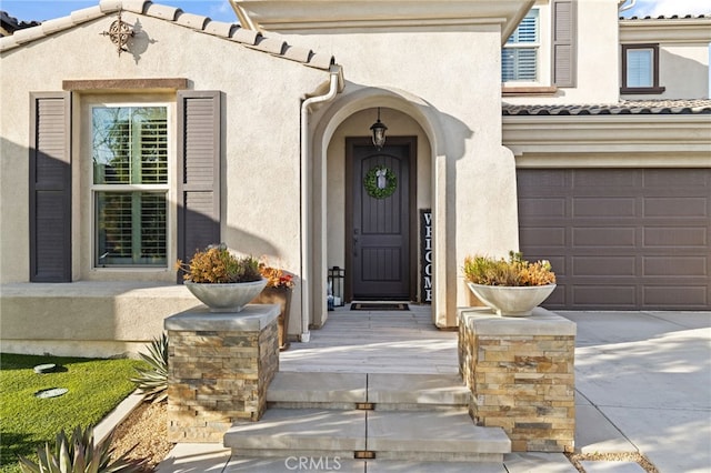 property entrance featuring stucco siding, driveway, a tile roof, and an attached garage