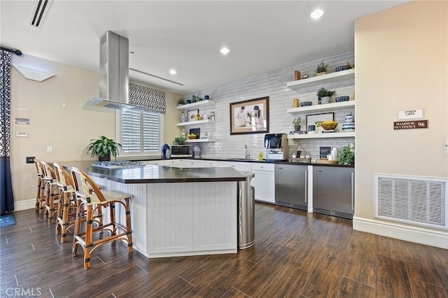 kitchen featuring dark countertops, open shelves, island range hood, dark wood-style floors, and a sink