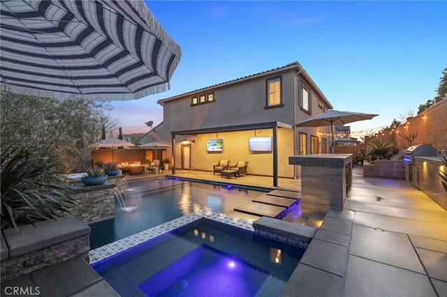 back of property at dusk with fence, area for grilling, a pool with connected hot tub, stucco siding, and a patio area