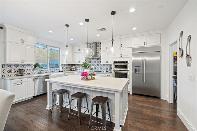 kitchen featuring visible vents, dark wood-style flooring, stainless steel appliances, white cabinets, and wall chimney range hood