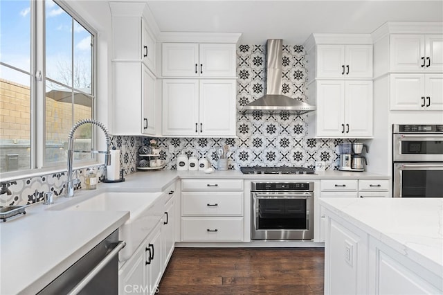 kitchen featuring appliances with stainless steel finishes, white cabinetry, wall chimney range hood, and dark wood-style flooring