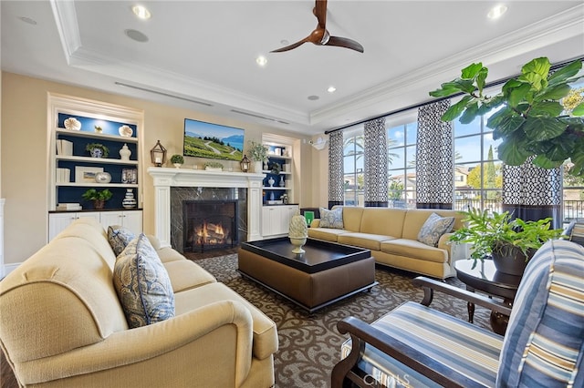 living area with built in shelves, a tray ceiling, recessed lighting, a high end fireplace, and crown molding