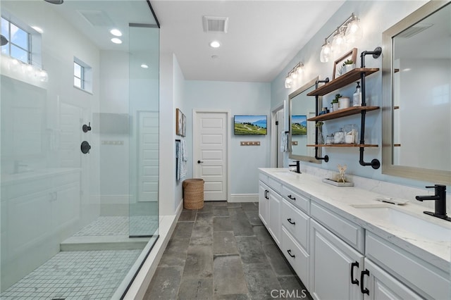 bathroom with double vanity, a walk in shower, visible vents, and a sink