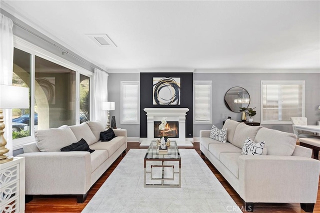 living area with dark wood-type flooring, a wealth of natural light, a warm lit fireplace, and visible vents