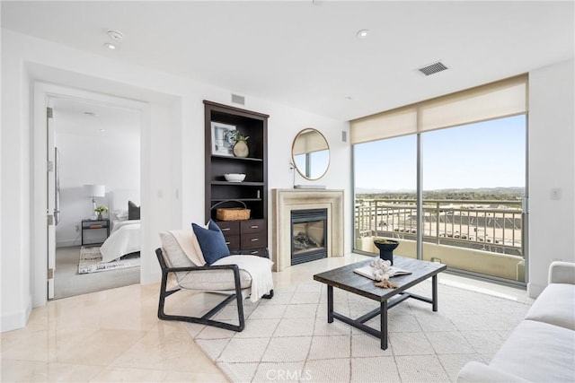 living area featuring built in features, a glass covered fireplace, and visible vents