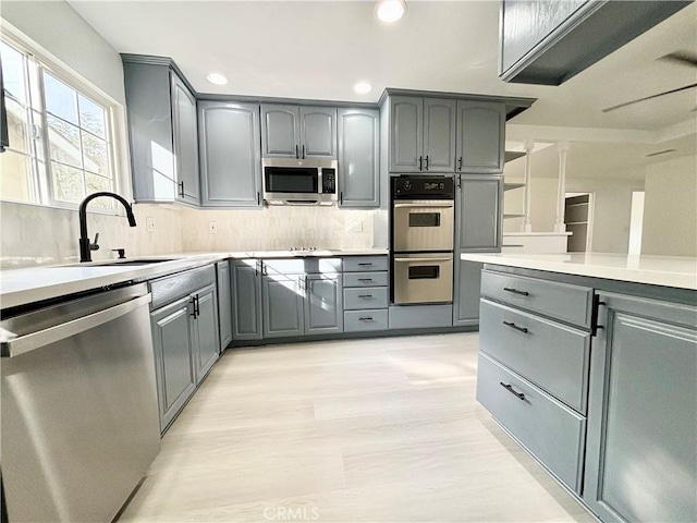 kitchen with light countertops, backsplash, gray cabinetry, appliances with stainless steel finishes, and a sink