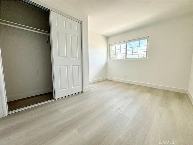 unfurnished bedroom featuring baseboards, a closet, and light wood-style floors