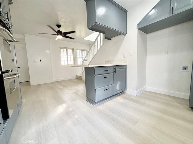 kitchen featuring light wood-style flooring, a peninsula, baseboards, light countertops, and gray cabinets