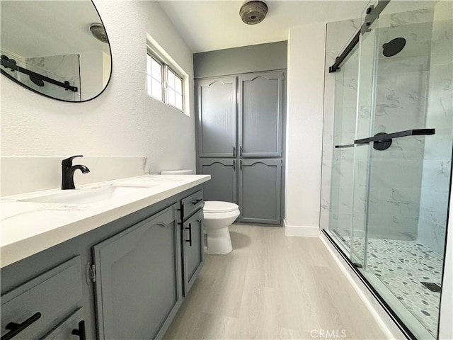 full bath featuring toilet, a marble finish shower, wood finished floors, and vanity