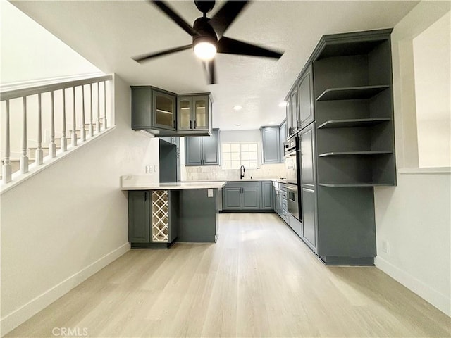 kitchen with light wood-style flooring, gray cabinetry, a peninsula, a sink, and baseboards