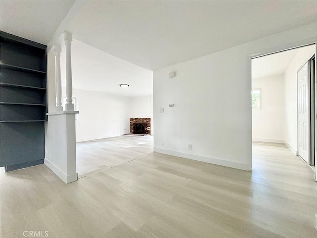 unfurnished living room with a brick fireplace, light wood-style flooring, and baseboards