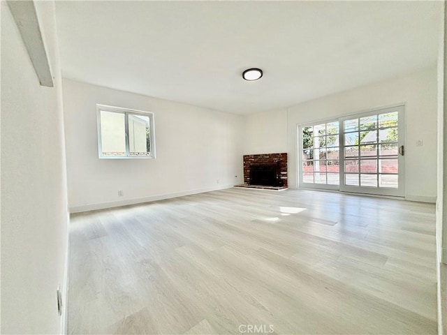 unfurnished living room featuring light wood-style flooring, a brick fireplace, a wealth of natural light, and baseboards