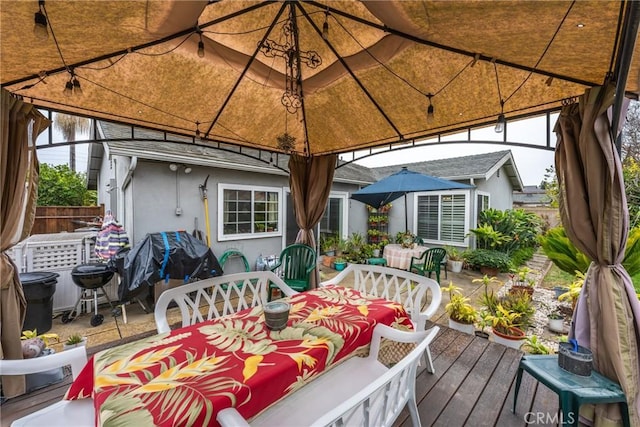 wooden terrace featuring a gazebo, outdoor dining area, and fence