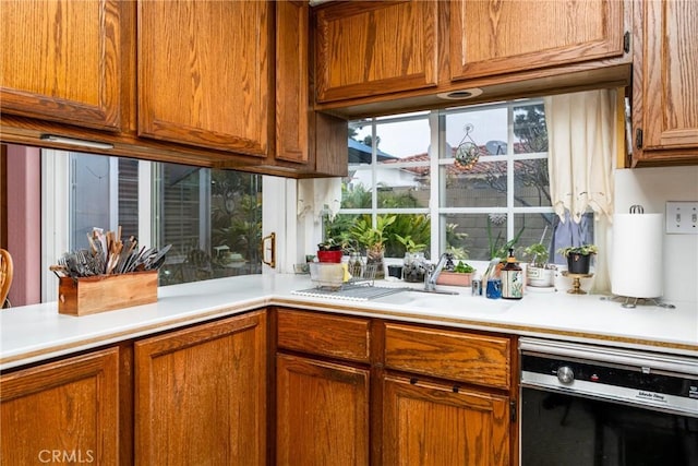 kitchen with brown cabinetry, light countertops, a sink, and dishwasher