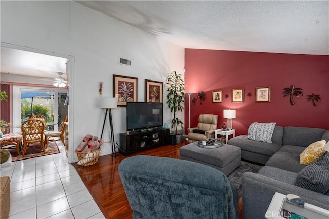 living room featuring lofted ceiling, ceiling fan, a textured ceiling, wood finished floors, and visible vents