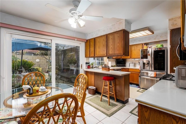 kitchen with light tile patterned floors, a peninsula, light countertops, stainless steel fridge with ice dispenser, and brown cabinetry