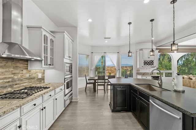 kitchen featuring light wood-style flooring, a sink, stainless steel appliances, wall chimney exhaust hood, and backsplash