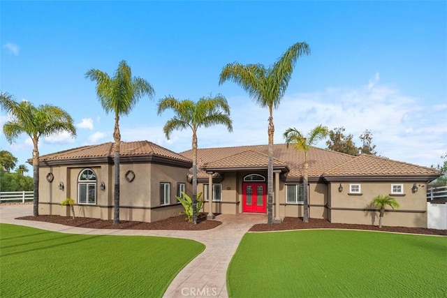 mediterranean / spanish-style house with fence, stucco siding, a front lawn, a tiled roof, and decorative driveway