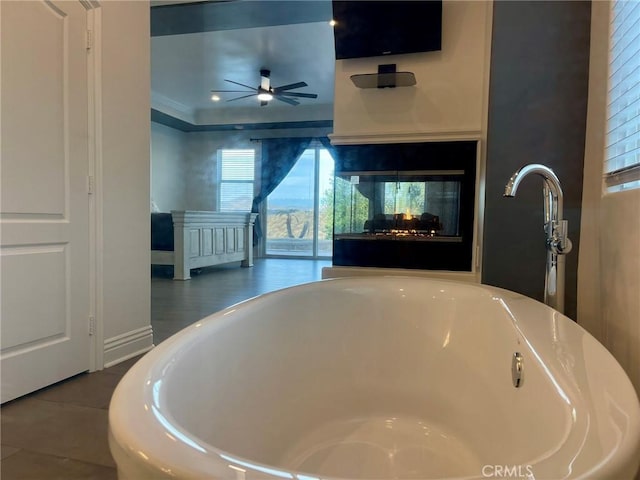 interior details featuring ceiling fan, a freestanding tub, a multi sided fireplace, and ornamental molding