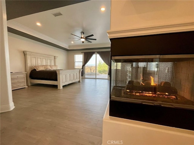 bedroom featuring visible vents, crown molding, a multi sided fireplace, wood finished floors, and access to outside